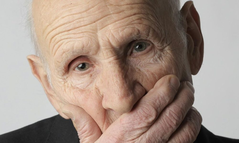older man in black suit covering his face