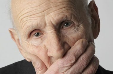 older man in black suit covering his face