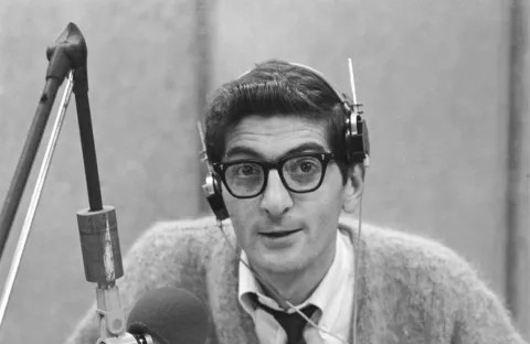 Dick Biondi wearing headphones sitting behind a microphone