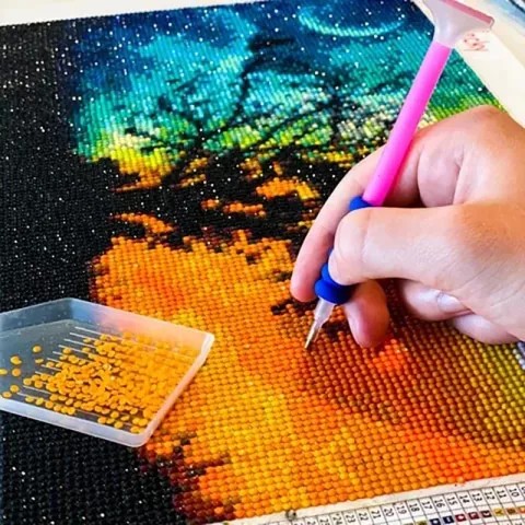 a hand holding a stylus doing diamond art work