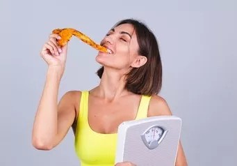 woman holding a scale while eating a slice of pizza