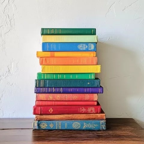 a stack of brightly colored books flat on a wooden table